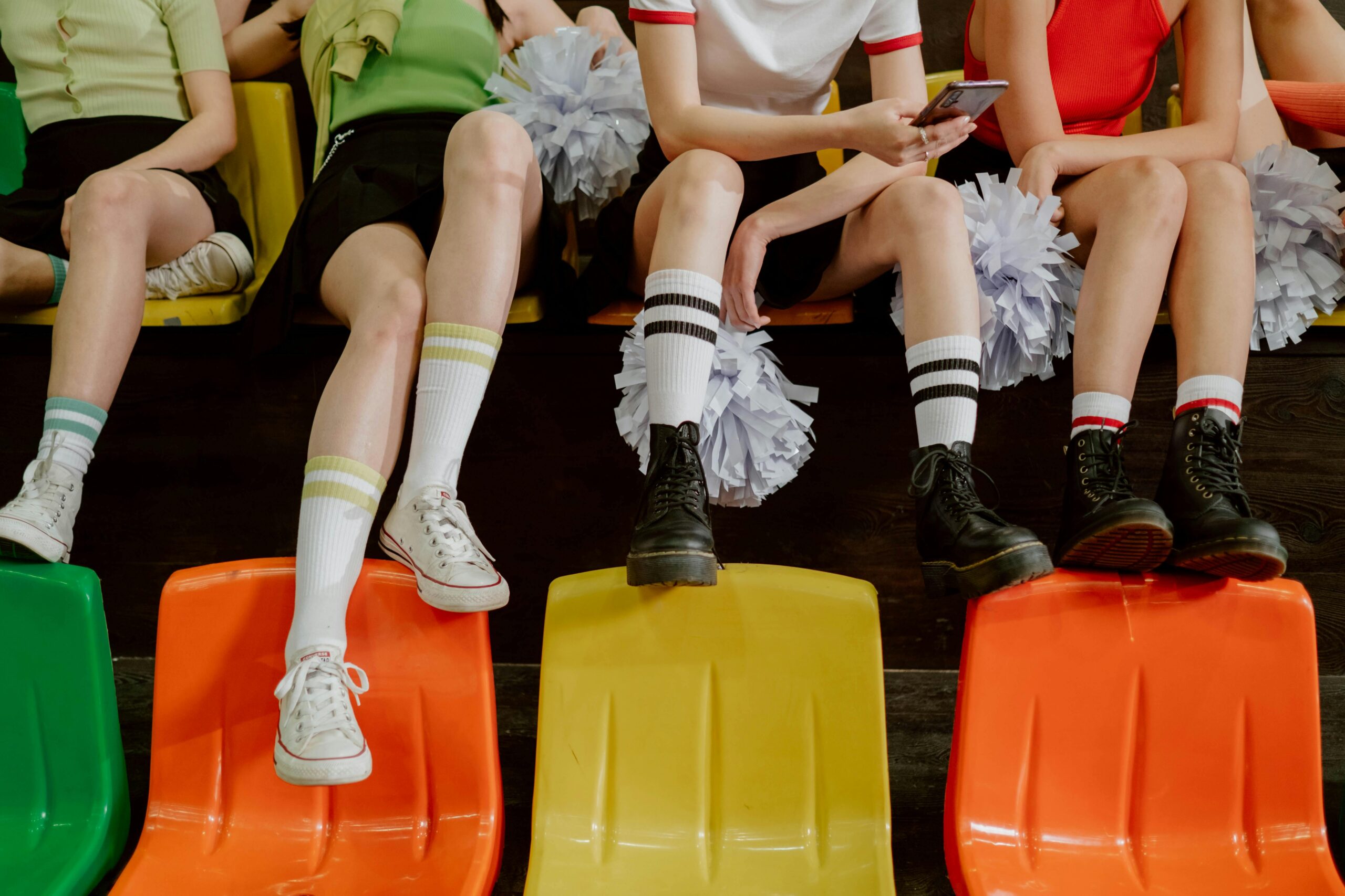 A group of cheerleaders sitting on colorful bleachers with pompoms during the day.